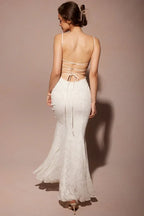 Back view of a woman wearing a white lace mermaid wedding dress with spaghetti straps and a low back with criss-cross ties, walking away.