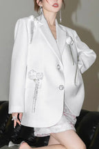 Close-up of a white blazer with floral and tassel accents.