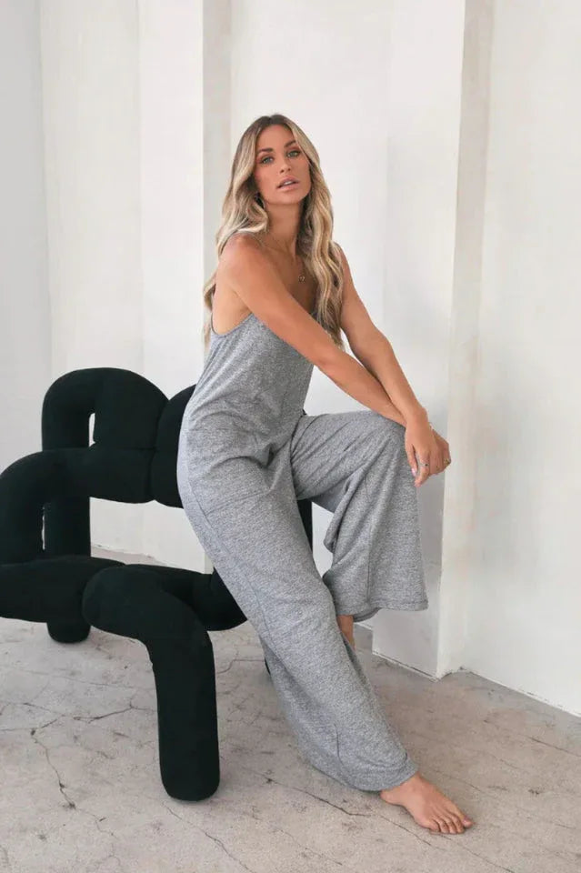 Woman wearing a grey wide leg jumpsuit, sitting on a modern black chair.