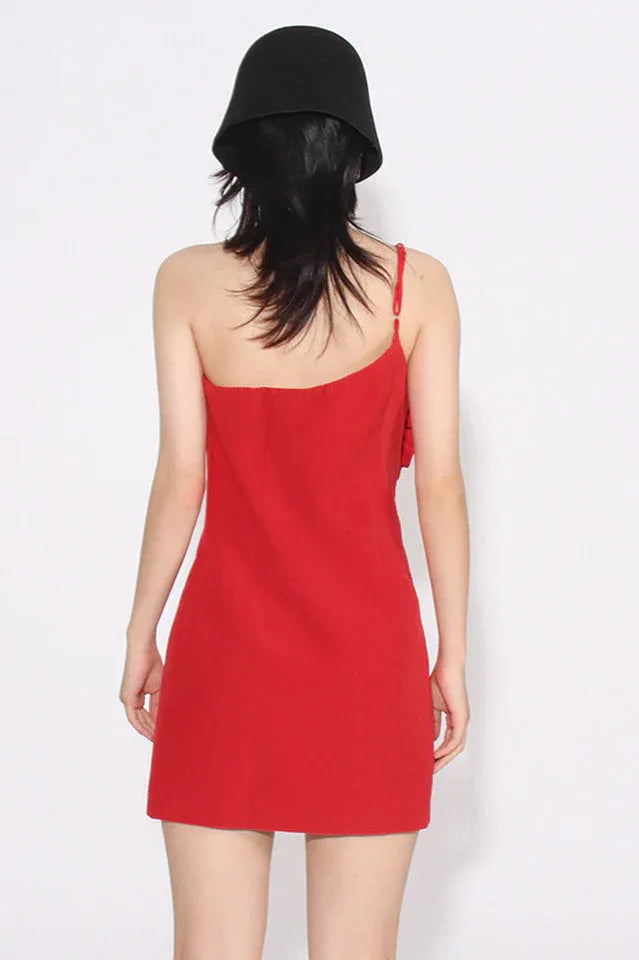 Back view of a red one-shoulder mini dress with a ruffled floral applique on the bust, worn by a woman with a black bucket hat.