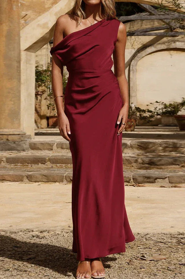 Full length portrait of a woman in a burgundy one-shoulder satin maxi dress.