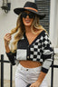 Woman wearing a black and white checkerboard print cropped cardigan with white jeans and a black hat.