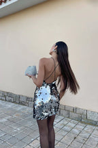 Rear view of a woman in a silver sequined halter mini dress, showing the open back and long dark hair.
