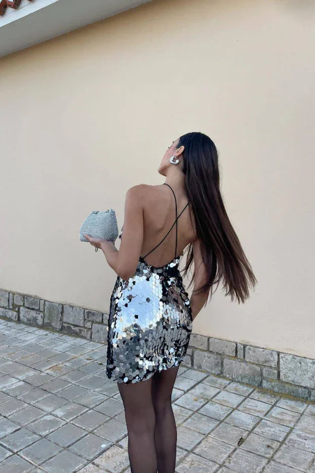 Rear view of a woman in a silver sequined halter mini dress, showing the open back and long dark hair.