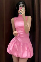 Woman taking a mirror selfie in a pink sleeveless mock neck dress with a bubble hem skirt.