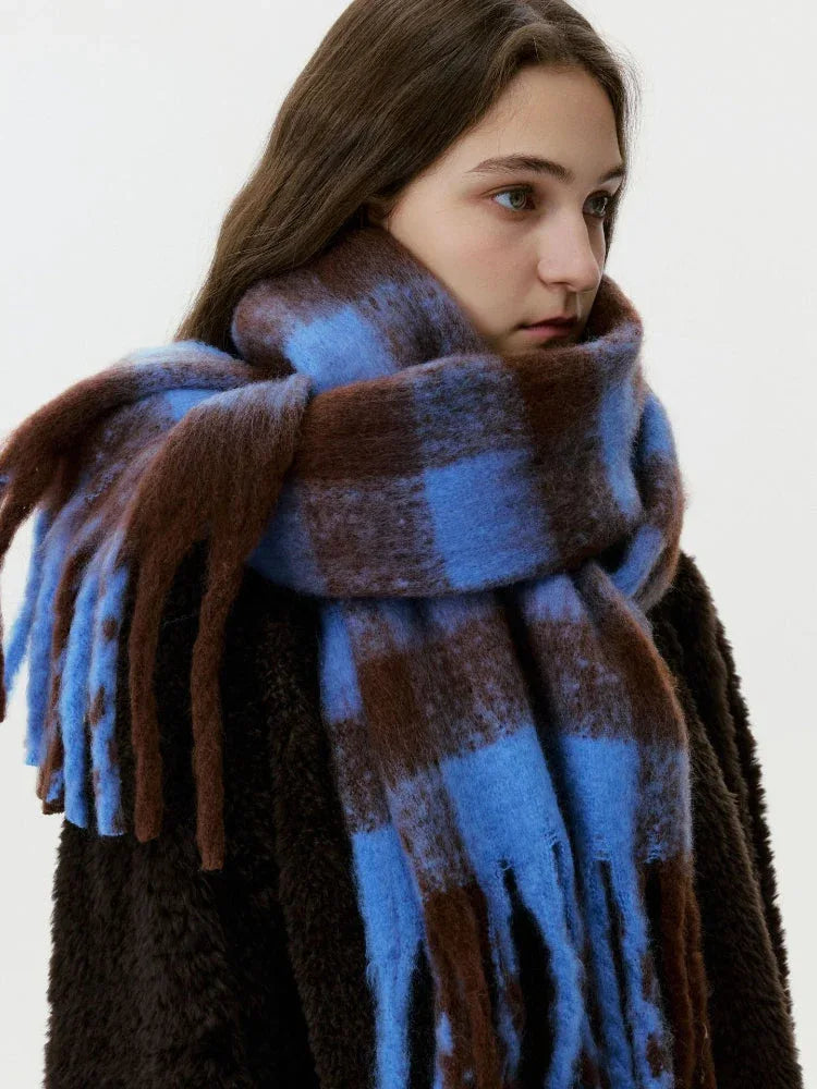 A woman wears a large, fuzzy, blue and brown plaid scarf with fringe details, draped around her neck and shoulders. Main image