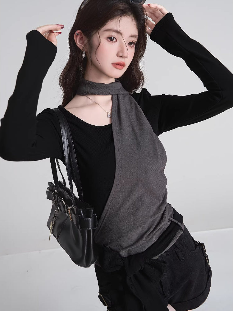 Woman wearing a black long-sleeved top with a grey asymmetrical overlay and scarf detail, with hands near her head.