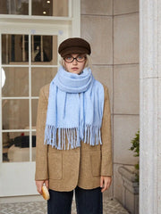 Front view of a young woman in a light blue fringed scarf and a brown tweed jacket.