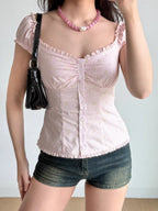 Woman wearing a pink striped and floral print top with denim shorts and a black handbag.