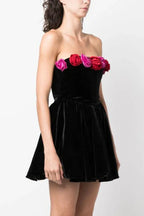 Side view of a woman wearing a black velvet strapless mini dress with floral trim.
