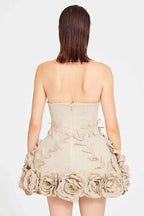 Back view of a woman wearing a strapless beige dress with a zipper closure. The skirt features a dense arrangement of fabric flowers around the hem.