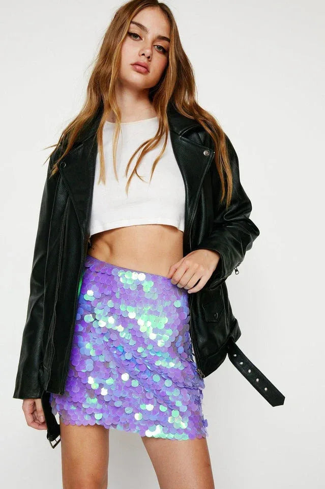 Woman wearing a black moto jacket over a white crop top and a purple iridescent sequin mini skirt. Main image