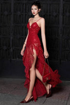 Woman wearing a red sequined lace evening gown with a high slit and ruffled hem, walking outdoors at night.