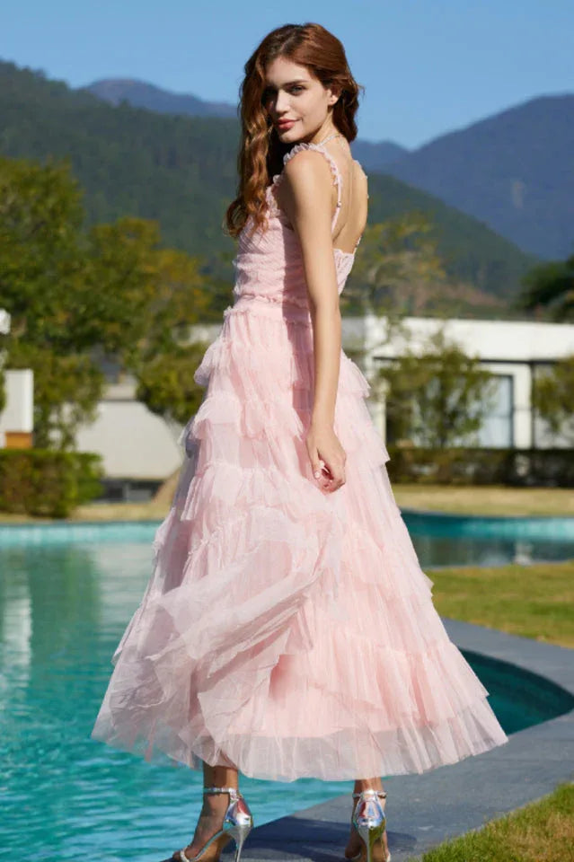 Rear view of a woman wearing a light pink tiered tulle dress with thin straps and a v-neckline.