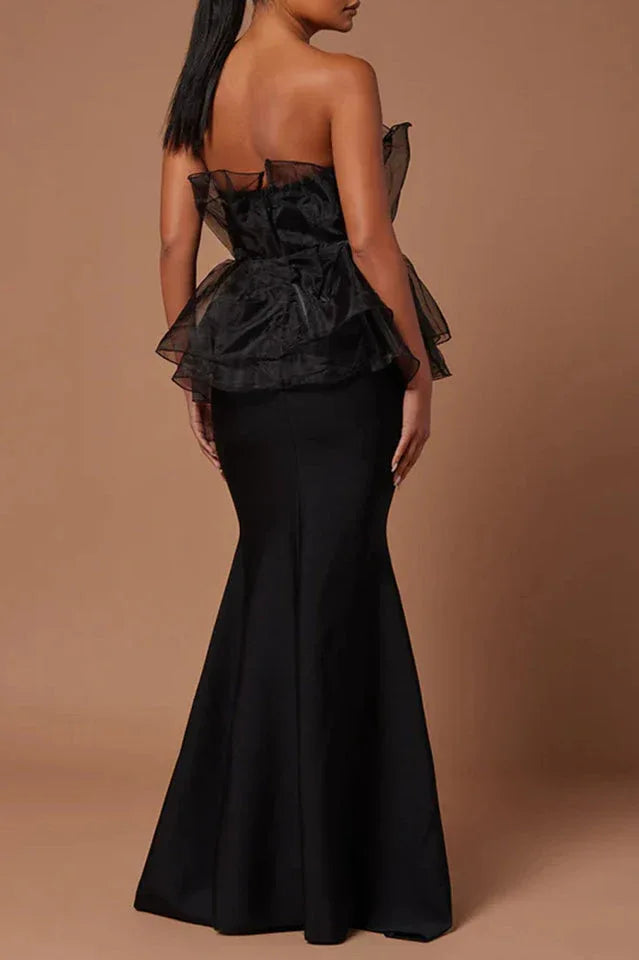Back view of a woman wearing a black strapless formal gown with a ruffled peplum bodice and mermaid skirt.