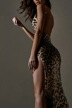 Back view of a woman in a leopard print satin maxi dress with a high slit, with her arm extended.