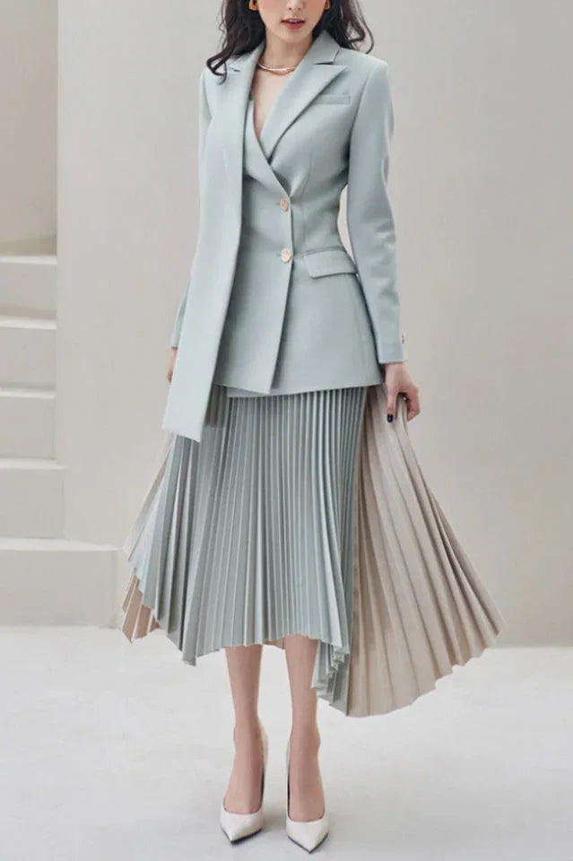 Woman wearing a light blue blazer and asymmetrical pleated skirt, standing. Main image