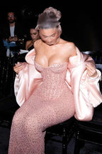 Woman wearing a pink sequined strapless gown with oversized pink satin sleeves and a sheer head covering, sitting down.