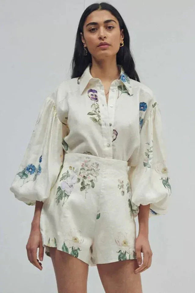 Woman wearing a white floral print button-down shirt with puffed sleeves and matching high-waisted shorts, front view Main image