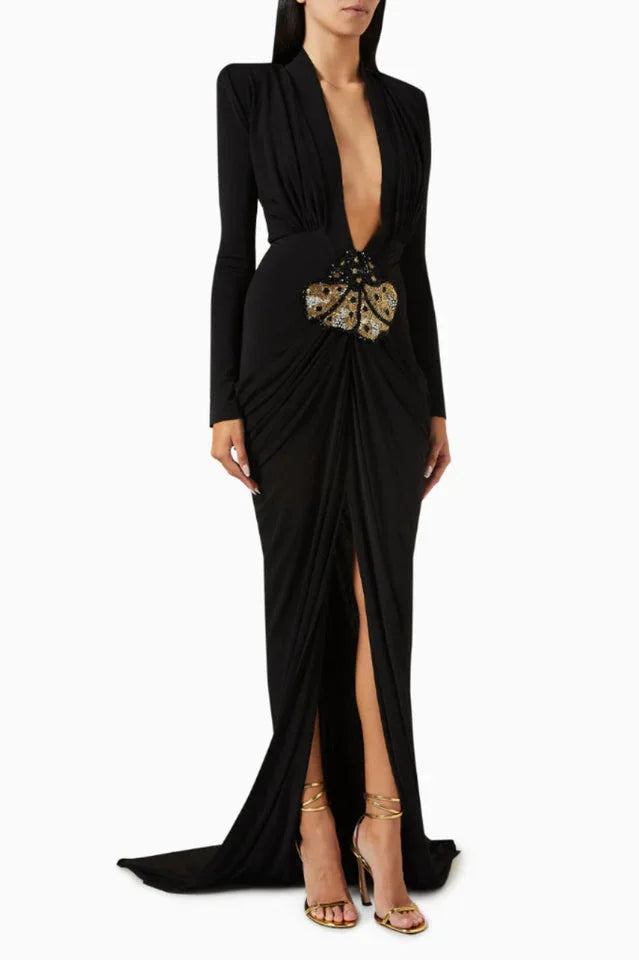 Full-length view of a black draped gown with a high slit, showcasing gold strappy heels and the butterfly embellishment.