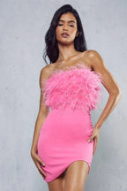 Woman posing in a pink strapless dress with feather trim on the bodice and an asymmetrical hem.
