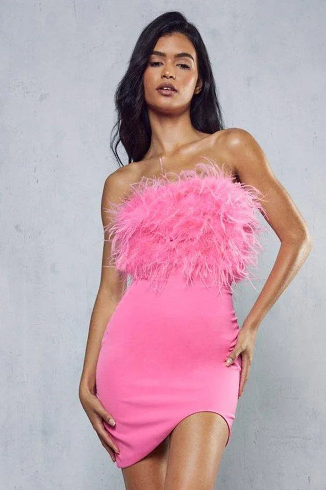 Woman posing in a pink strapless dress with feather trim on the bodice and an asymmetrical hem.