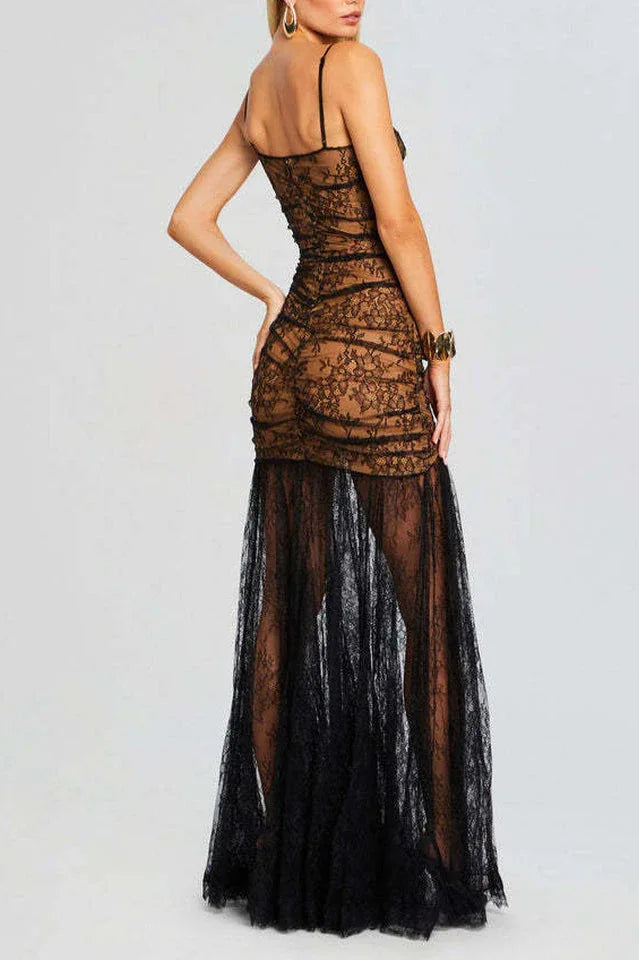 Rear view of a woman in a floor-length black lace dress with a sheer overlay and a high slit.