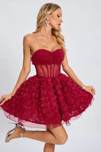 Full-body shot of a woman posing in a short, strapless red dress with a floral applique skirt and metallic heels.
