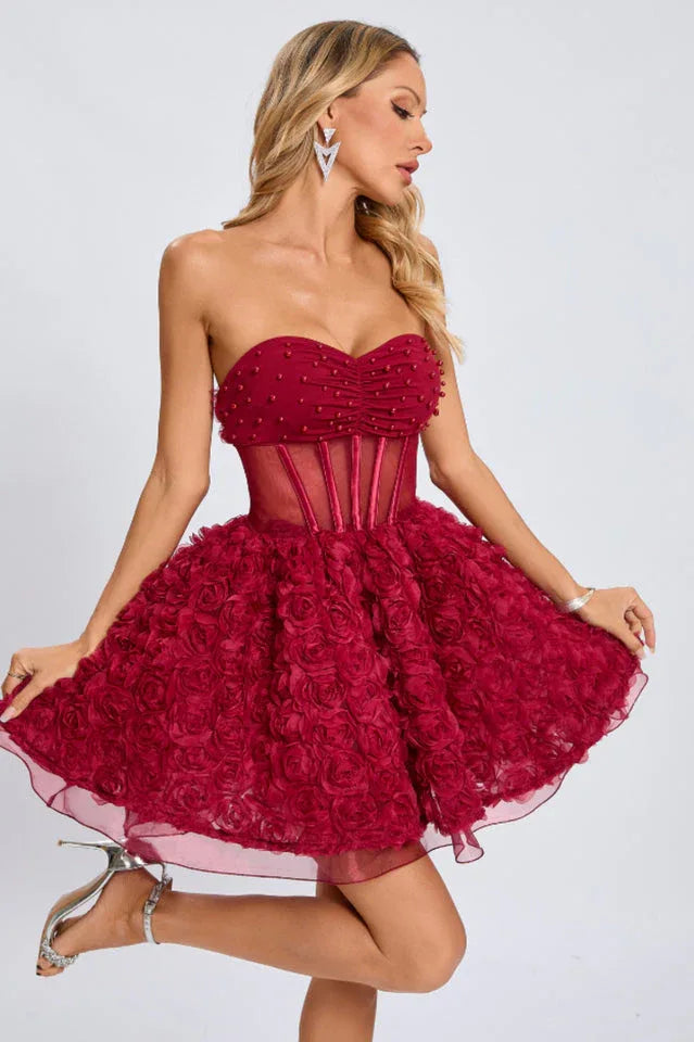 Full-body shot of a woman posing in a short, strapless red dress with a floral applique skirt and metallic heels.