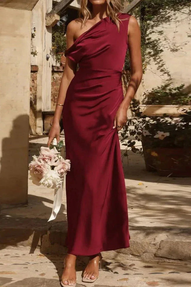 Woman wearing a burgundy one-shoulder satin maxi dress, holding a bouquet of flowers. Main image