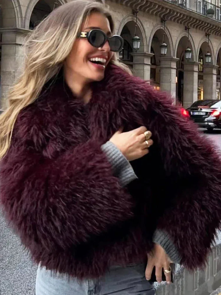 Woman wearing a burgundy shaggy faux fur cropped jacket, laughing and showing her ring.