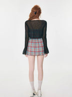 Back view of a woman wearing a plaid mini dress and a sheer black cardigan.