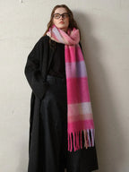 A woman poses with a vibrant, striped scarf draped over her dark outerwear.
