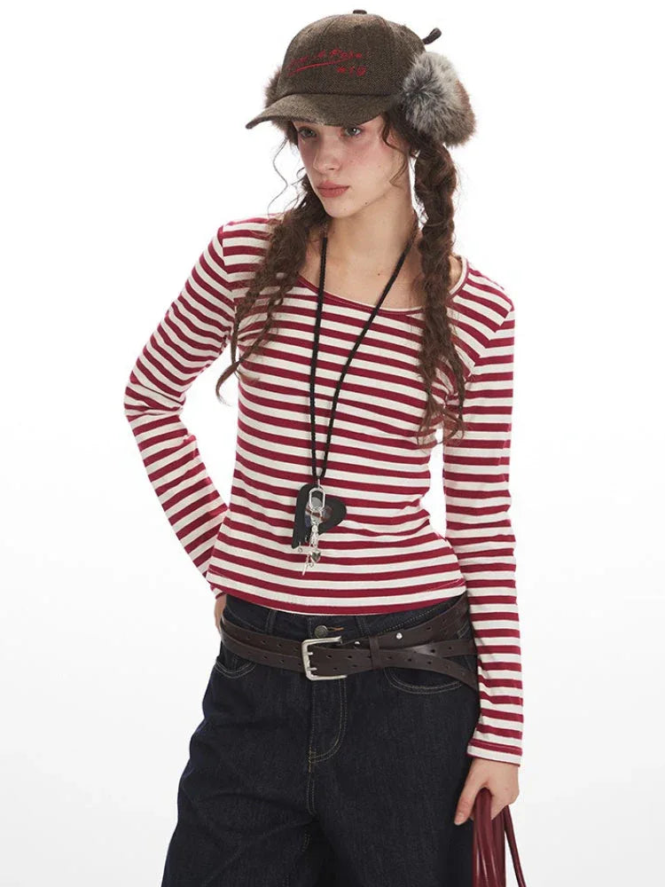 Close-up of a woman's upper body wearing a red and white striped long-sleeved shirt, a necklace with a black heart pendant, and a fur-trimmed hat.