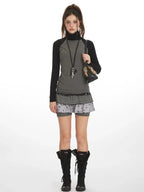 Model wearing a gray and black long-sleeve turtleneck top with a layered skirt and black boots, front view.