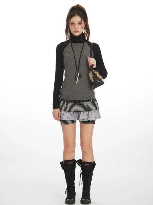 Model wearing a gray and black long-sleeve turtleneck top with a layered skirt and black boots, front view.
