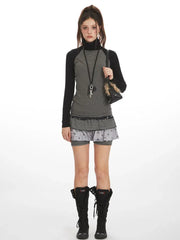 Model wearing a gray and black long-sleeve turtleneck top with a layered skirt and black boots, front view.