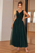 Woman in a floor-length dark green sequined and tulle formal dress with a v-neckline, adjusting the skirt.