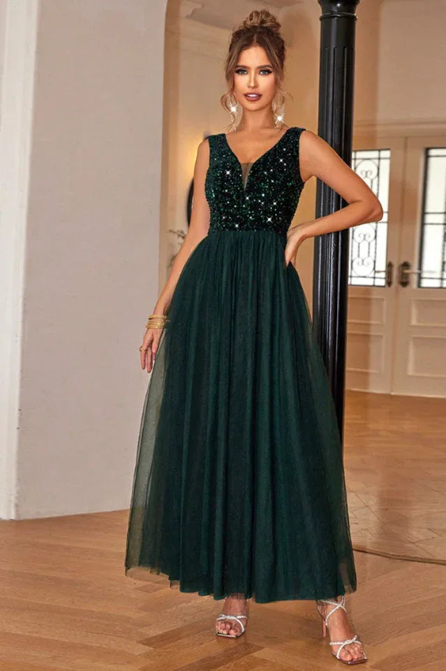 Woman in a floor-length dark green sequined and tulle formal dress with a v-neckline, adjusting the skirt.