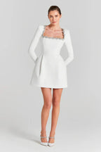 Full-length view of a woman in a white A-line mini dress with long sleeves and embellished neckline.
