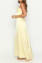 side view of a woman wearing a pale yellow satin maxi dress with spaghetti straps and a sweetheart neckline, showing the slit