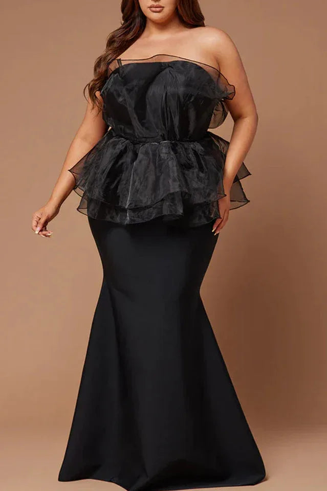 Plus-size woman wearing a black strapless formal gown with a ruffled peplum bodice and mermaid skirt.