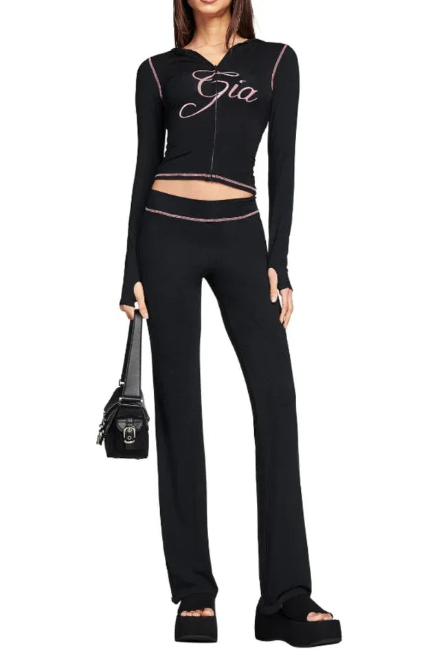 Full outfit view of a black long-sleeve zip-up top with pink embroidery and matching flared pants, held by a model with a black handbag.