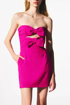 Model posing in a vibrant pink strapless mini dress with bow accents.