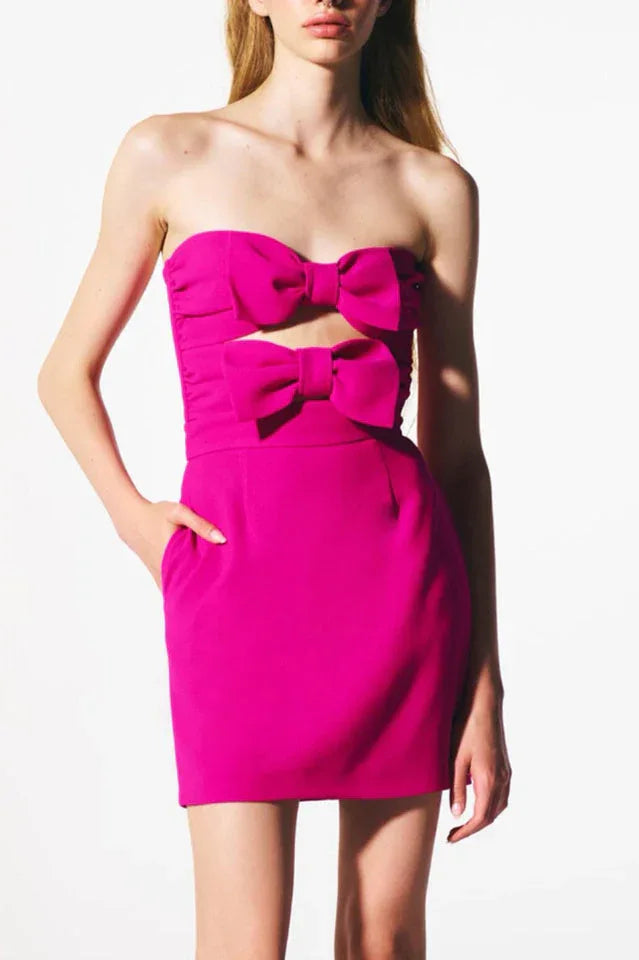 Model posing in a vibrant pink strapless mini dress with bow accents.