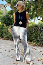 Woman from the side wearing a black sleeveless top and black and white striped wide leg pants, holding a straw tote bag.