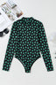 A black long-sleeved mesh bodysuit with a green shamrock print laid flat, with sunglasses and a magazine nearby.