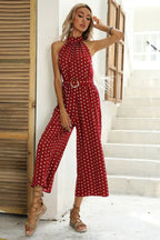 Woman wearing a red polka dot halter neck wide leg jumpsuit with a belt.