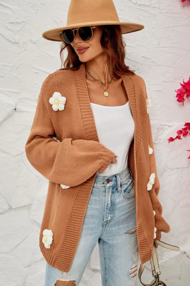 Woman wearing a brown floral cardigan and ripped jeans, with a hat and sunglasses.
