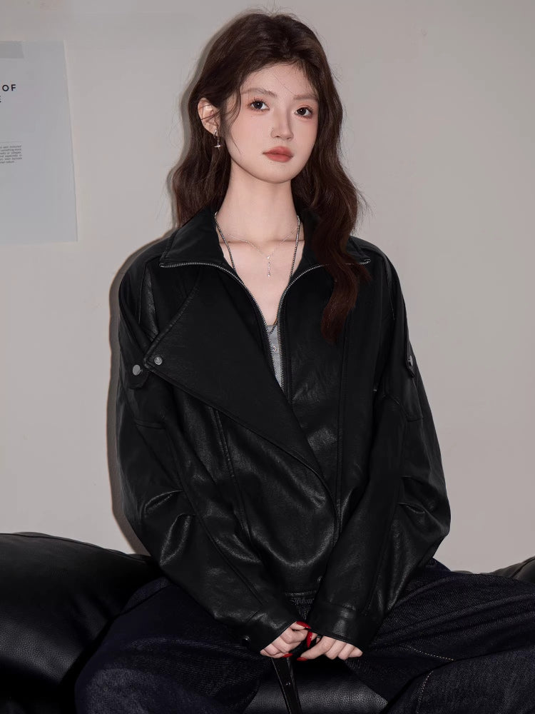 Woman wearing a black faux leather jacket with lapel collar and asymmetrical zipper, paired with a grey crop top and dark wash jeans.
